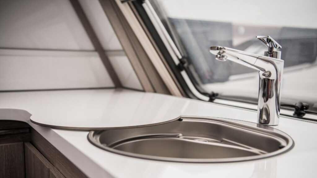 RV technician repairing under-sink pipes inside a motorhome parked in a Denver driveway