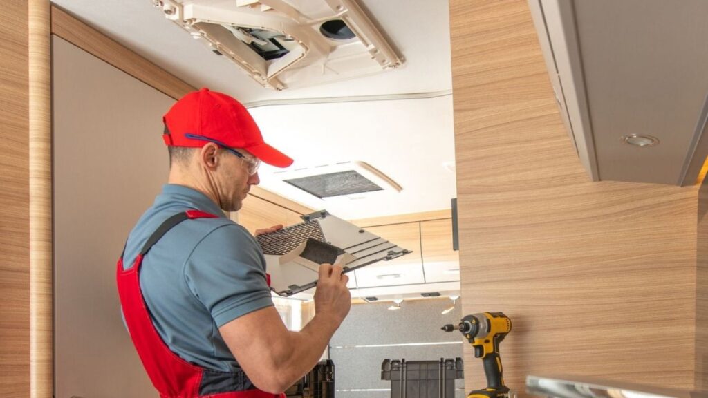 Technician repairing rooftop RV air conditioner at Denver campground